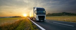 White truck arriving on the asphalt road in rural landscape at sunset